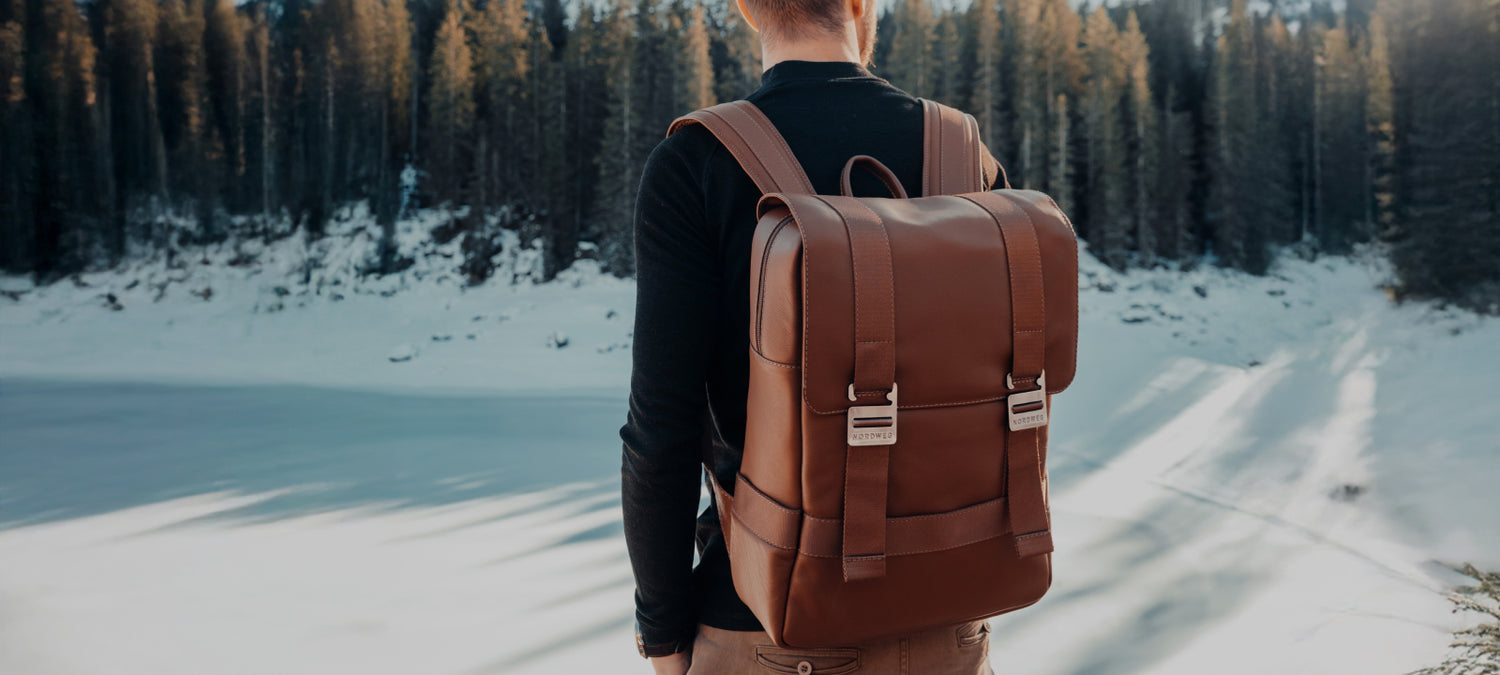 Caramel Nordweg Dolomites leather backpack worn on a snowy forest trail, desktop homepage hero crop
