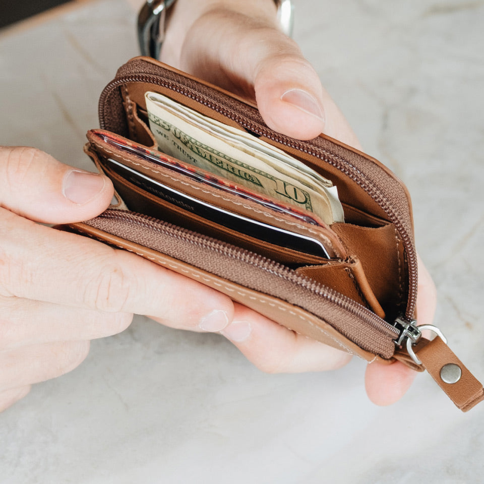 Brown leather wallet with money held open by a hand on a neutral background