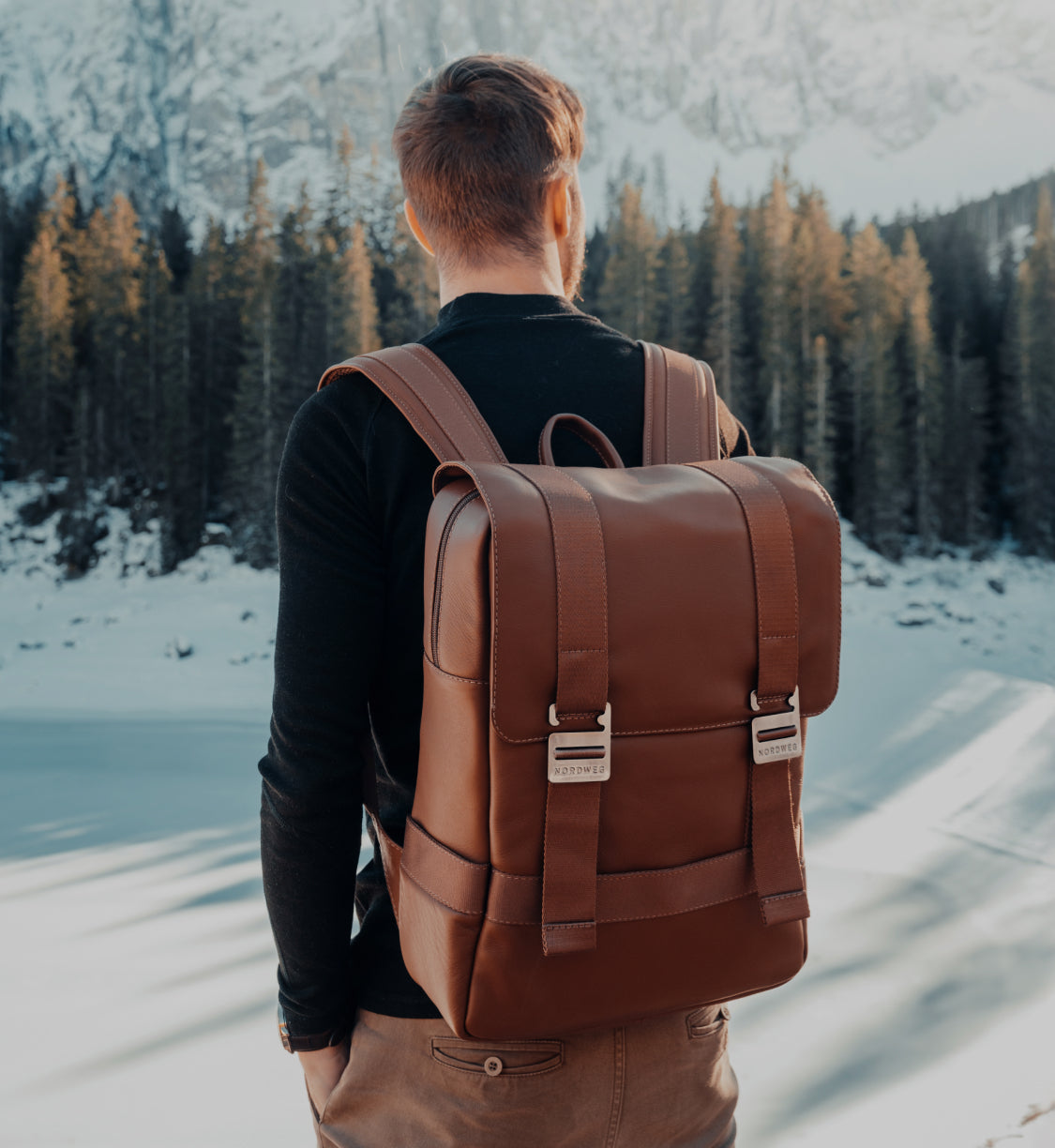 Caramel Nordweg Dolomites leather backpack worn on a snowy forest trail, mobile homepage hero crop