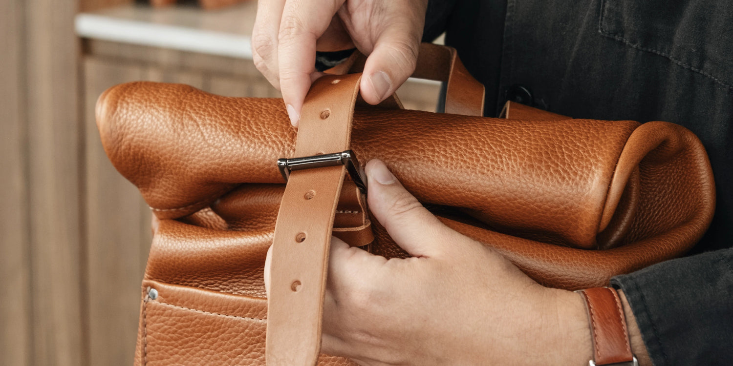 Close-up of the cognac leather closure strap and metal buckle on the Nordweg Legacy Leather Backpack