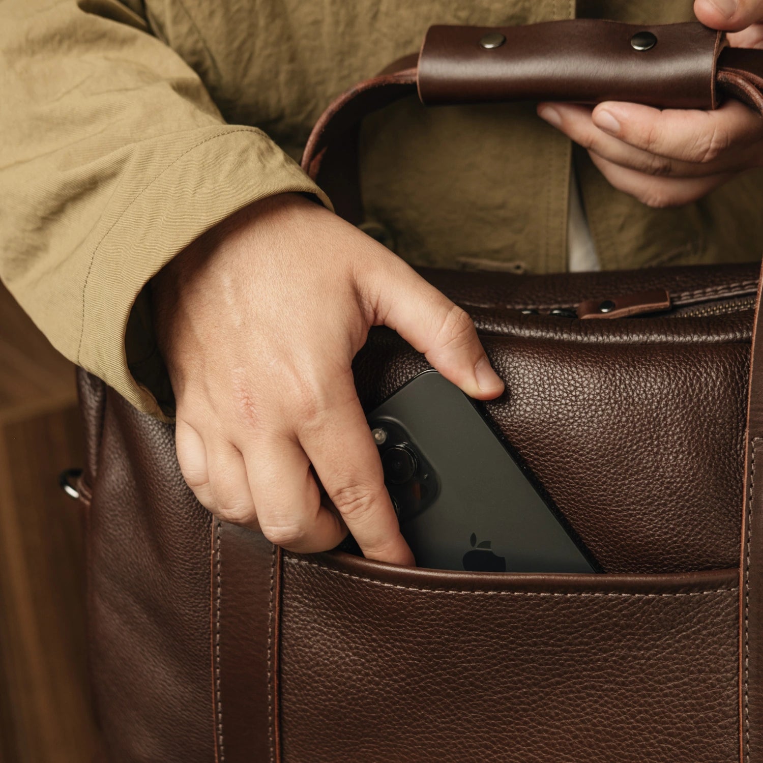 Hand sliding a smartphone into the side pocket of the Nordweg Legacy Leather Briefcase in espresso